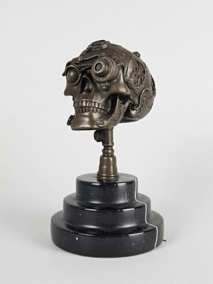 tête de squelette en bronze posée sur un socle en marbre noir, sur fond blanc