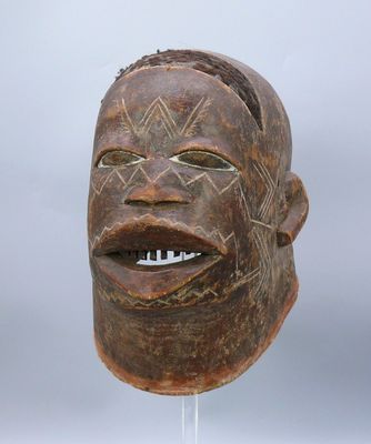 une image représentant un masque en bois posé sur un socle, sur fond gris