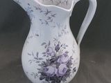 un pichet blanc orné de fleurs violettes, posé sur une table