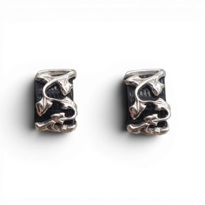 une paire de boucles d'oreilles noires et argentées posées sur une surface blanche