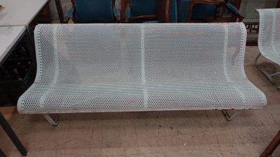 un banc en métal blanc dans une pièce où se trouvent des chaises bleues