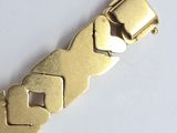 a gold plated bracelet with a metal clasp on a white surface