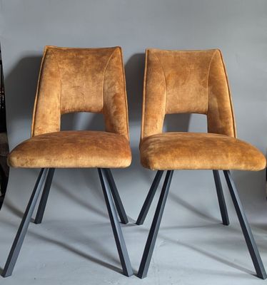 pair of brown leather chairs with metal legs against a gray wall