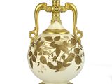 a white and gold vase with a gold handle on a white surface