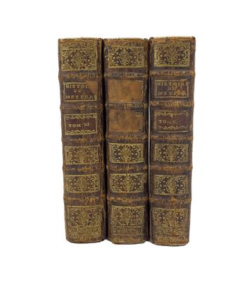 trois vieux livres sont empilés sur une surface blanche