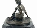 bronze statue of a woman sitting on a rock on a white background