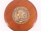 une photo d'une plaque en bois sur laquelle est apposé un médaillon en bronze