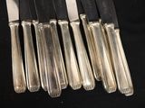 six silverplated knives are lined up on a black surface