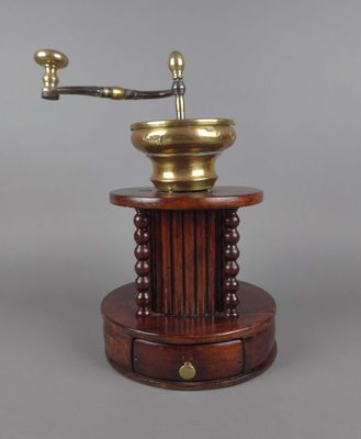 un moulin à café ancien posé sur un socle en bois et muni d'une poignée en métal