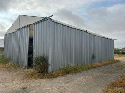 un grand bâtiment métallique dont la porte est ouverte, donnant sur un chemin de terre