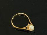 bague en or avec une perle au centre, sur un fond noir