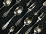 de nombreuses cuillères et fourchettes en argent posées sur un fond noir
