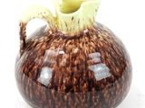 un vase marron et blanc, muni d'une anse jaune sur un fond blanc