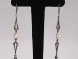 a pair of pearl and silver earrings on a black stand