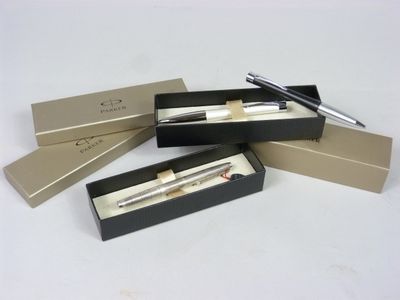 trois stylos dans une boîte posée sur une table, dans laquelle se trouve un stylo