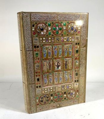 un livre en or richement décoré, sur lequel figure l'image d'une femme entourée de bijoux et de pierres précieuses
