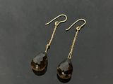 une paire de boucles d'oreilles pendantes en quartz fumé posées sur un fond noir