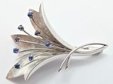 silver brooch with blue stones on it on a white surface