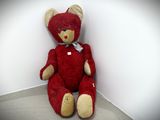 a red teddy bear sitting against a white wall