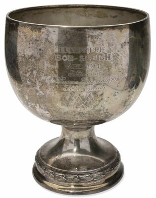 une coupe en argent ancienne posée sur un socle, sur fond blanc