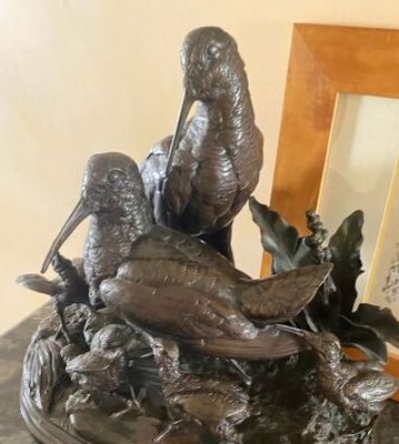 une statue représentant un oiseau posé sur une table, à côté d'un cadre photo