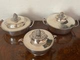 three silver dishes on a wooden table with a white wall in the background