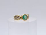 gros plan d'une bague en or avec une pierre verte et des diamants