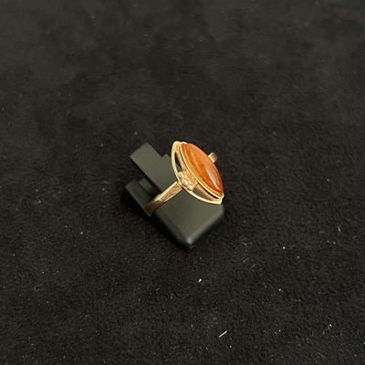 an image of a ring with an orange stone on a black surface