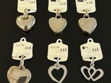 six silver heart charms with price tags on them sitting on a table