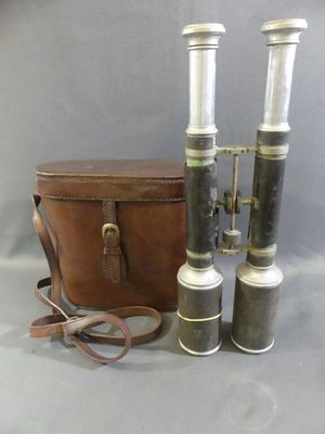 two silver and black binoculars and a brown bag on a gray surface