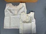 two pieces of white clothing on a bed next to a wooden shelf