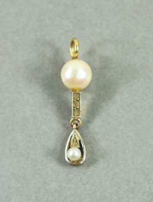 un gros plan d'un pendentif en perle et diamant posé sur une surface grise