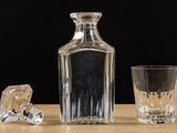 a glass and a decanter sitting on a table next to a shot glass