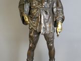 statue en bronze représentant un homme coiffé d'un chapeau et vêtu d'un manteau, posée sur un socle