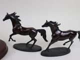 two figurines of horses running on a white surface
