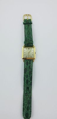 un gros plan d'une montre avec un bracelet vert posée sur une surface blanche