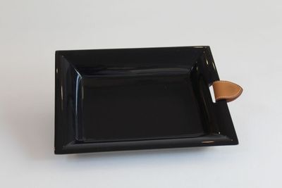 une petite assiette noire avec un manche en bois posée sur une table blanche
