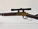 un vieux fusil avec un canon en bois et une lunette de visée, posé sur un socle en acrylique transparent