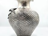 a silver vase with a flower on it on a white surface