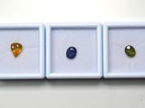 trois pierres précieuses de couleurs différentes se trouvent dans une boîte blanche posée sur une surface blanche
