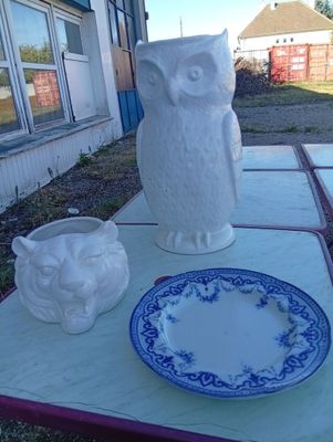 une statue de chouette blanche posée sur une table, à côté d'une assiette bleue et blanche