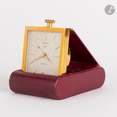 une petite horloge posée dans un écrin rouge sur une surface blanche