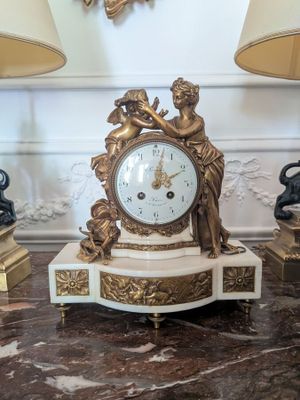 une horloge en or posée sur une table en marbre, flanquée de deux lampes