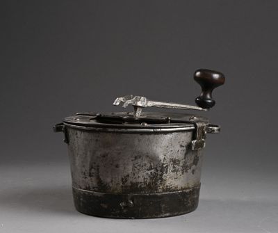 une vieille casserole en métal avec une poignée en bois posée sur une surface grise
