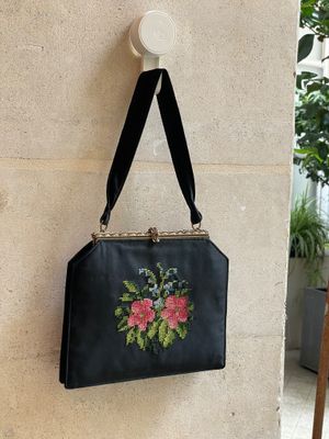 un sac à main noir orné de broderies florales, accroché au mur à côté d'une plante en pot