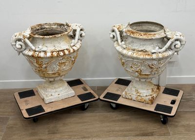 une paire d'urnes anciennes en fonte, posées sur des pieds en fonte, sur un sol en bois