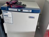 un réfrigérateur blanc sur lequel sont posés des gants, à côté d'une chaise rouge
