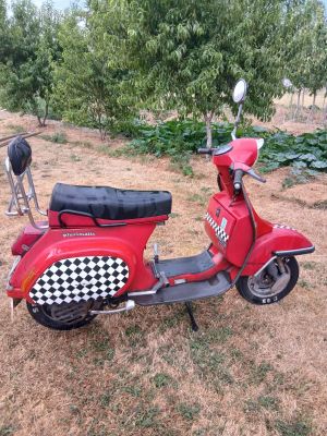 un scooter rouge avec une selle à carreaux, garé dans un champ