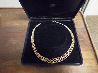 un collier en or dans un écrin noir posé sur une table en bois