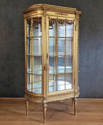 une vitrine ancienne dorée avec des portes vitrées, posée sur un parquet